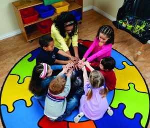 techer sitting on floor with student. they are sitting in a circle with their arms in the middle of the circle