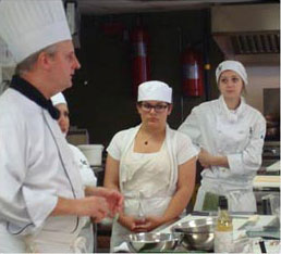 2 female students listening to chef in kitchen