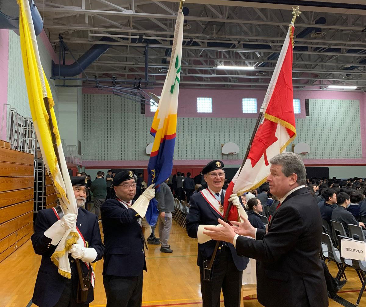 Members of the Knights of Columbus honour guard who are holding flags talk at the back of the gym before the beginning of Mass. 