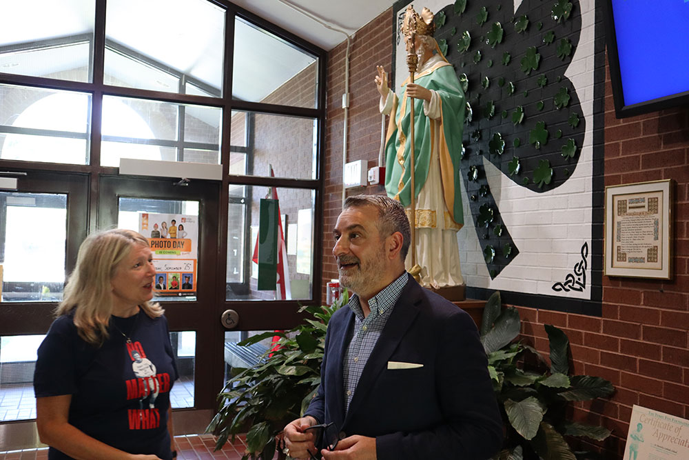 Minister Calandra and Principal Pellegrini talk in the foyer of St. Patrick CES Markham with a statue of St. Patrick in the background. 