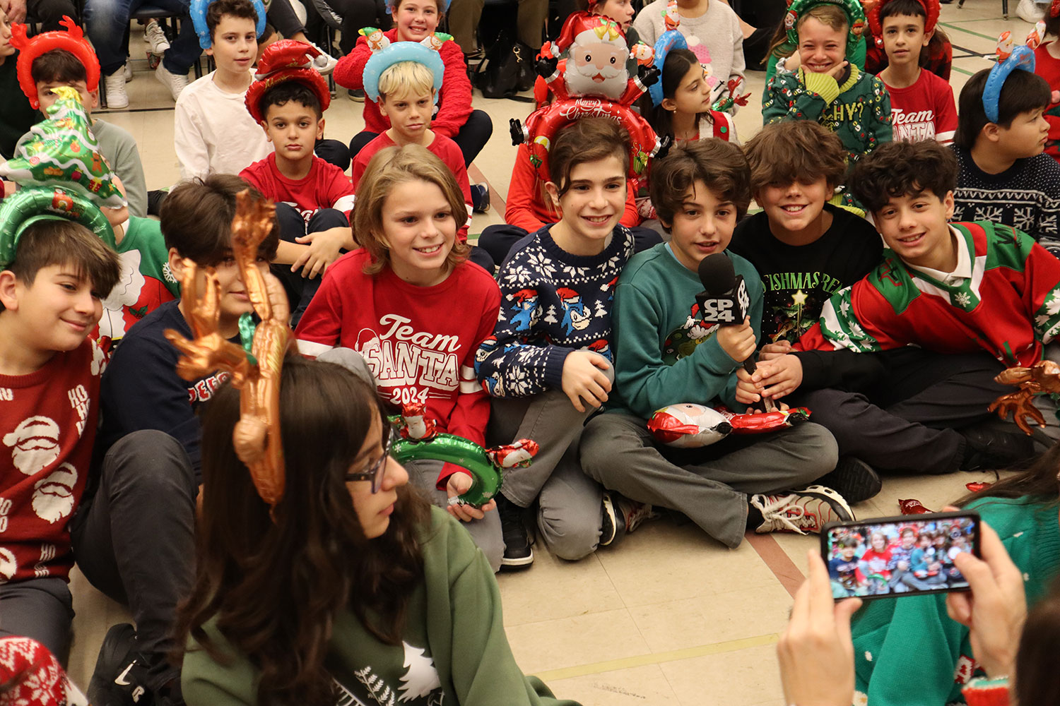 Grade 5 and 6 students dressed in Christmas-themed sweaters posing for a picture while holding a CP24 microphone.