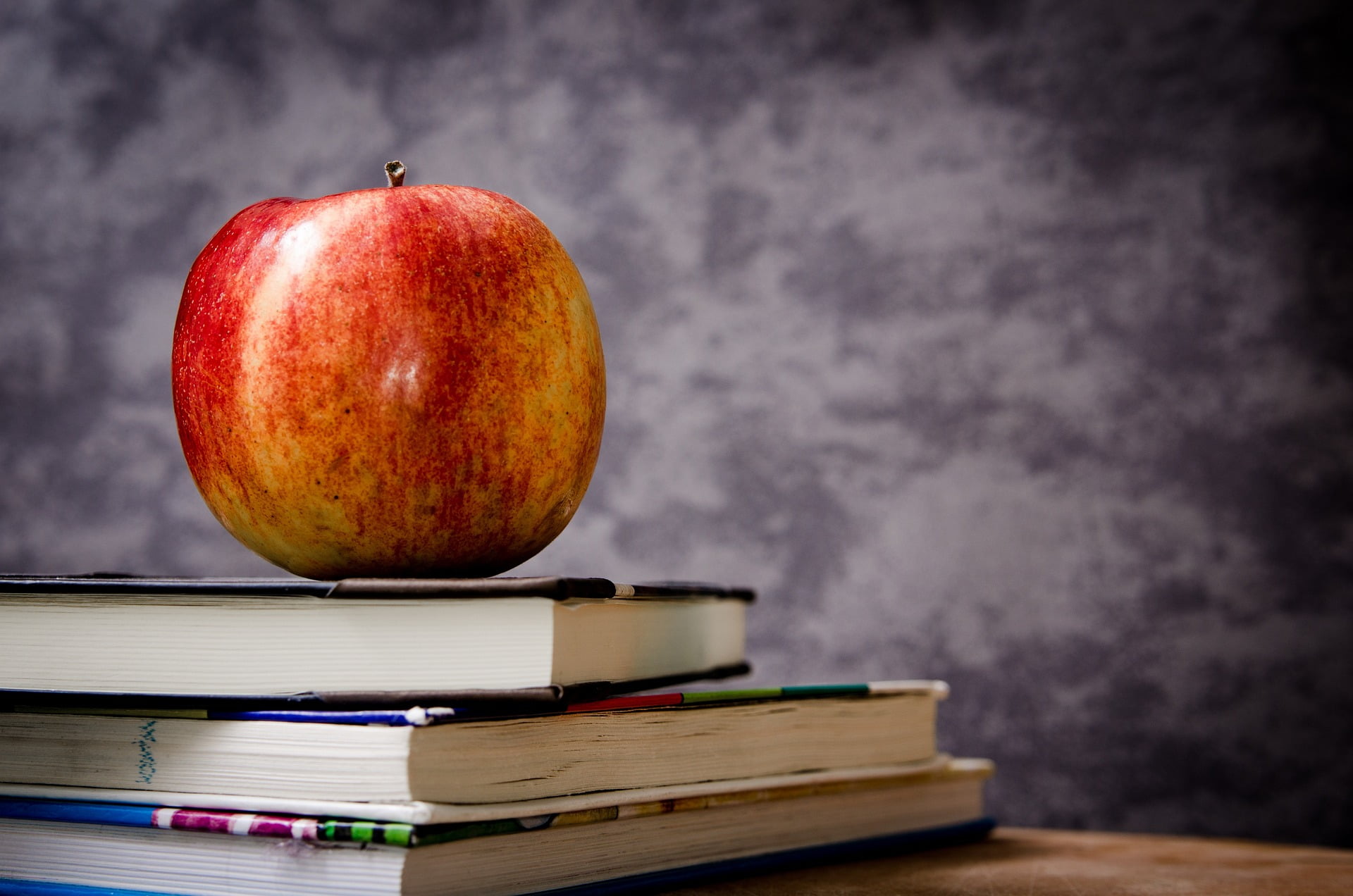 Apple sits on top of a stack of books with a chalkboard in the background