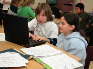 two students sti in front of a laptop in a classroom setting